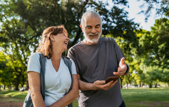 A mature couple laughing while on a walk, looking at mobile phone.