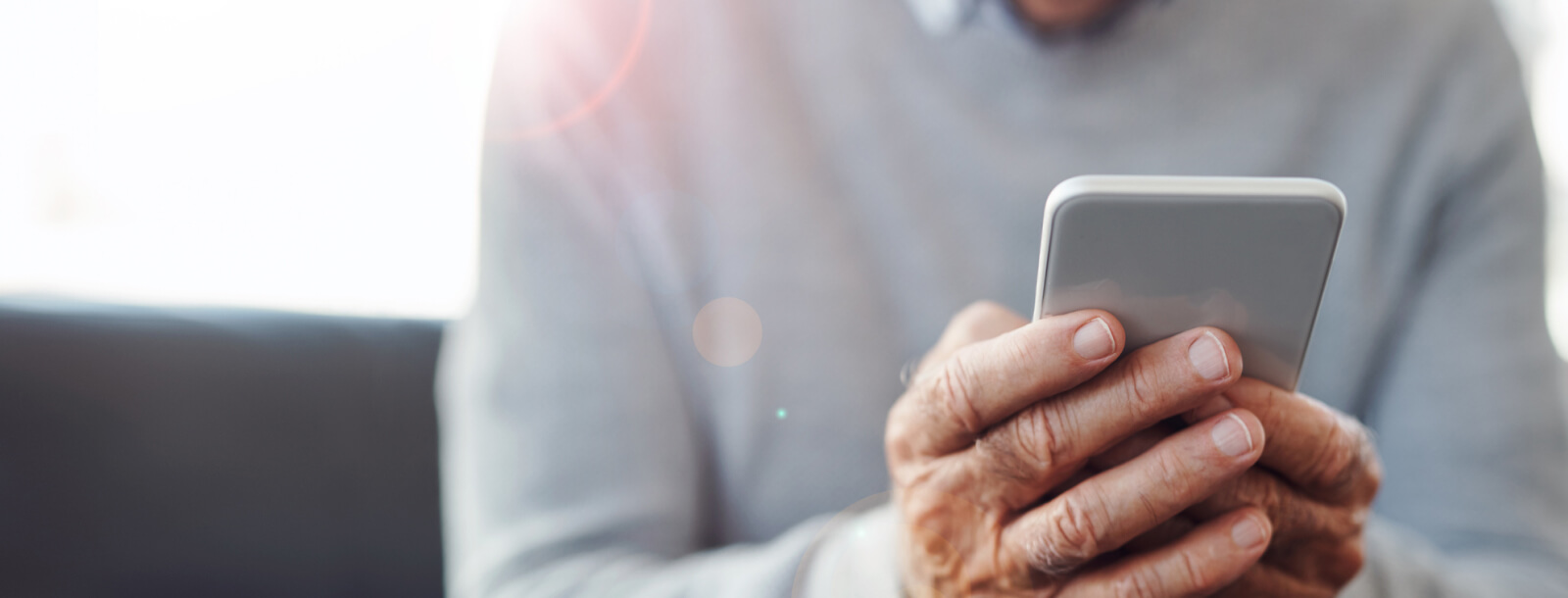 Hands of mature man using mobile phone while sitting